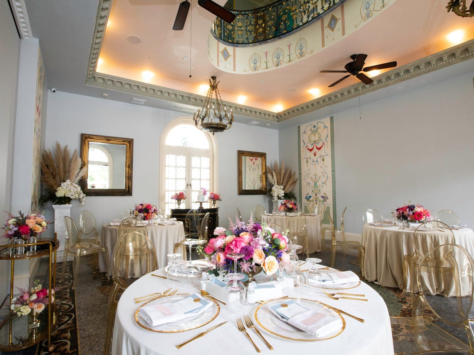 South Florals centerpieces on round banquet tables in an event venue dining room with ghost chairs and a painted ceiling.