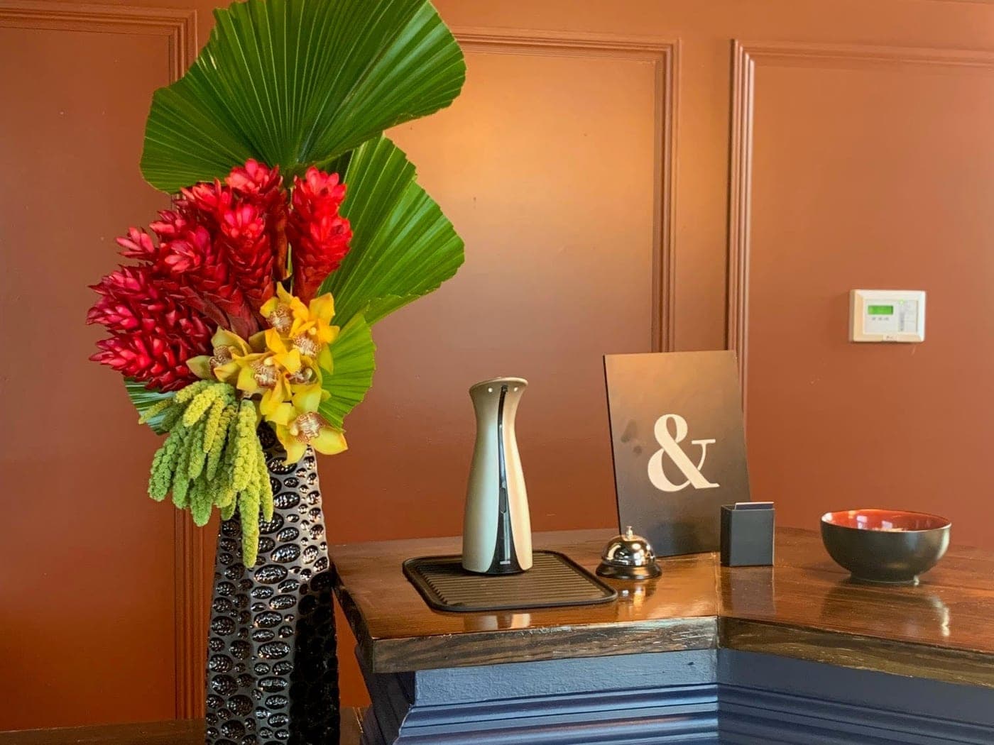 Tall South Florals arrangement of red ginger, orchids and fan palm beside a reception desk.