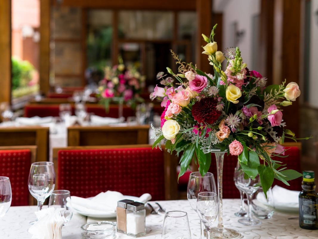 Mixed pink, burgundy and cream floral centerpiece on a table in a restaurant dining room.